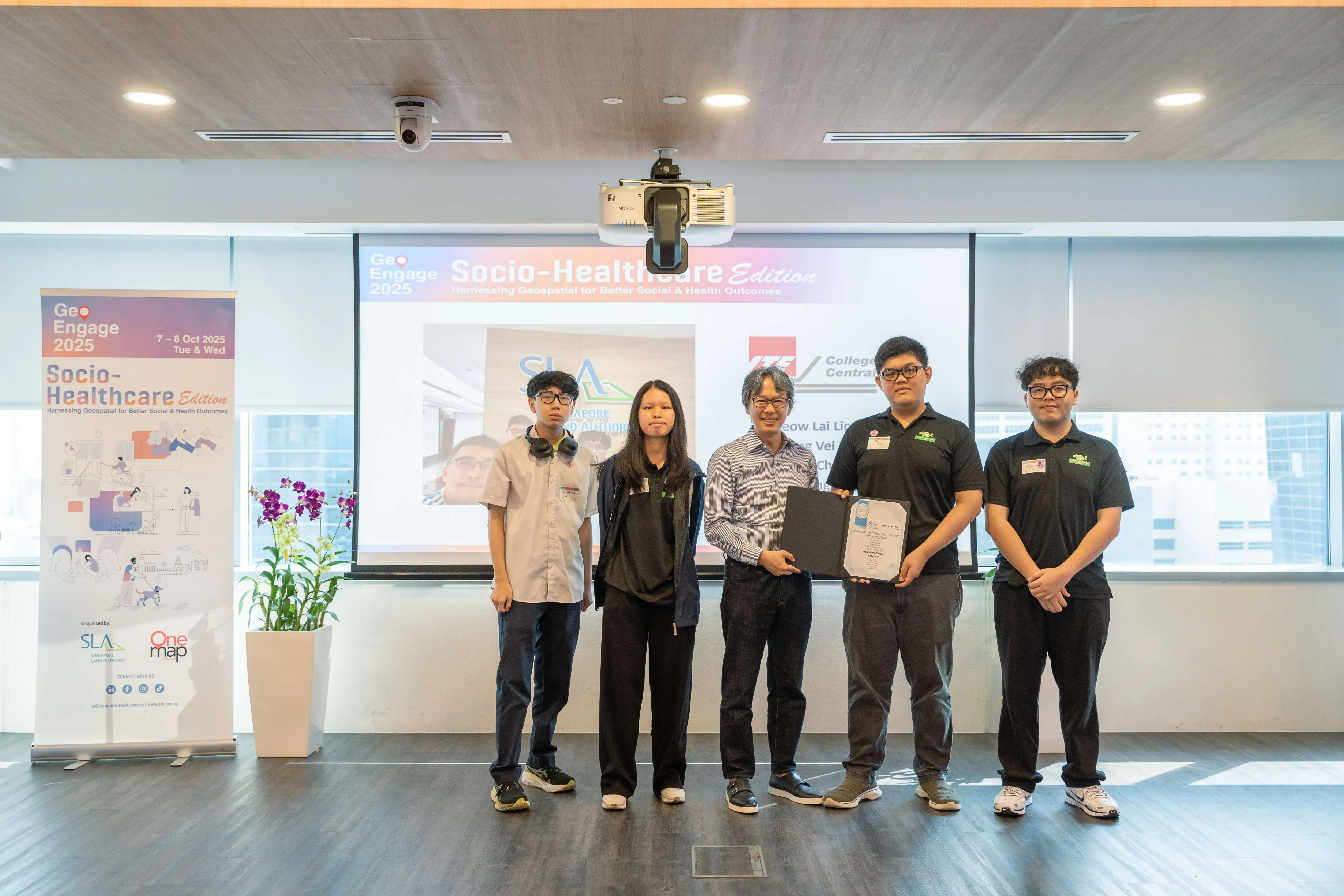 Certificate presentation for AWS-SLA Geospatial Innovation Challenge at the GeoEngage 2025 Socio-Healthcare Edition event, one holding a certificate.